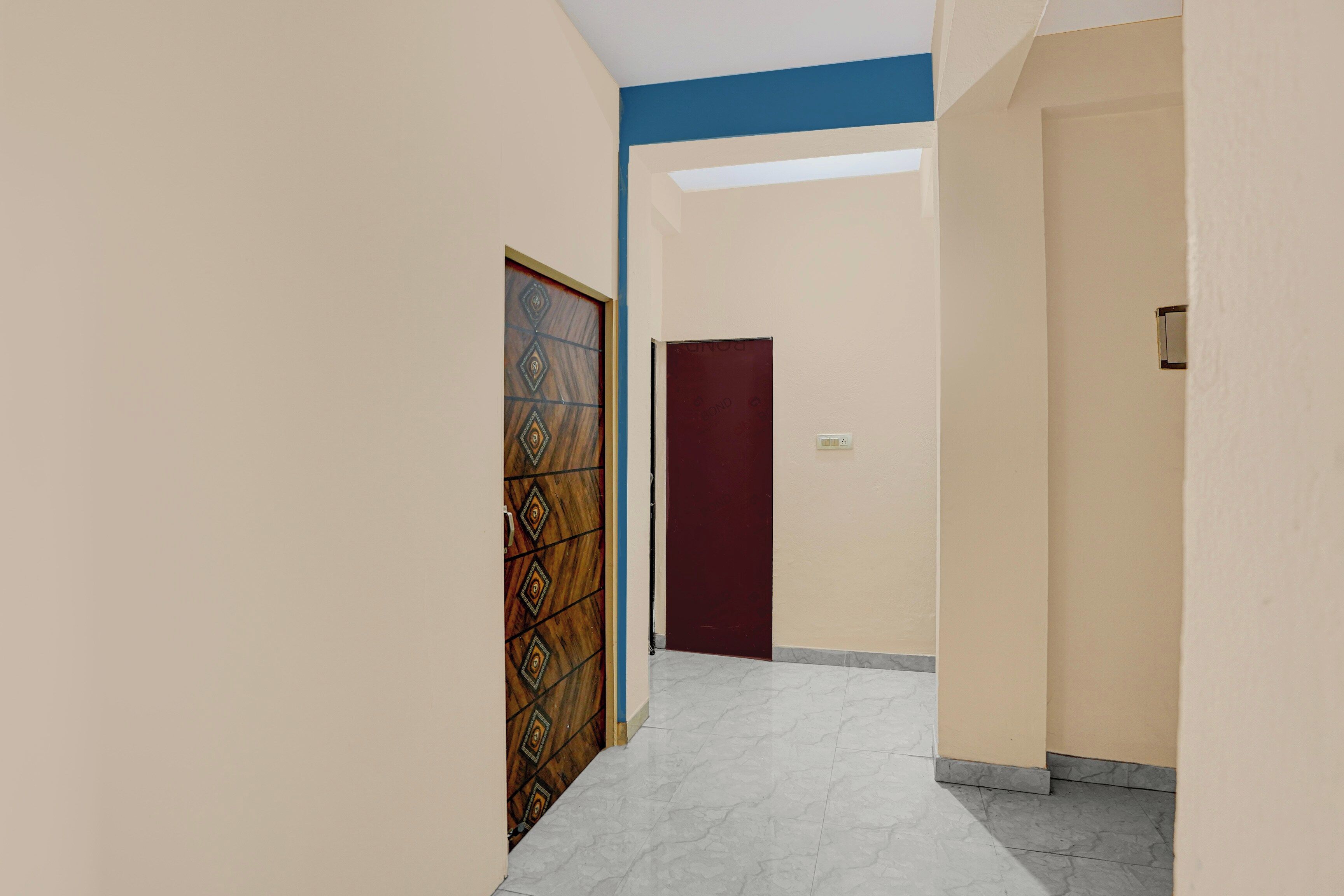 Um corredor com uma porta estampada, uma porta lisa e um interruptor de luz na parede.