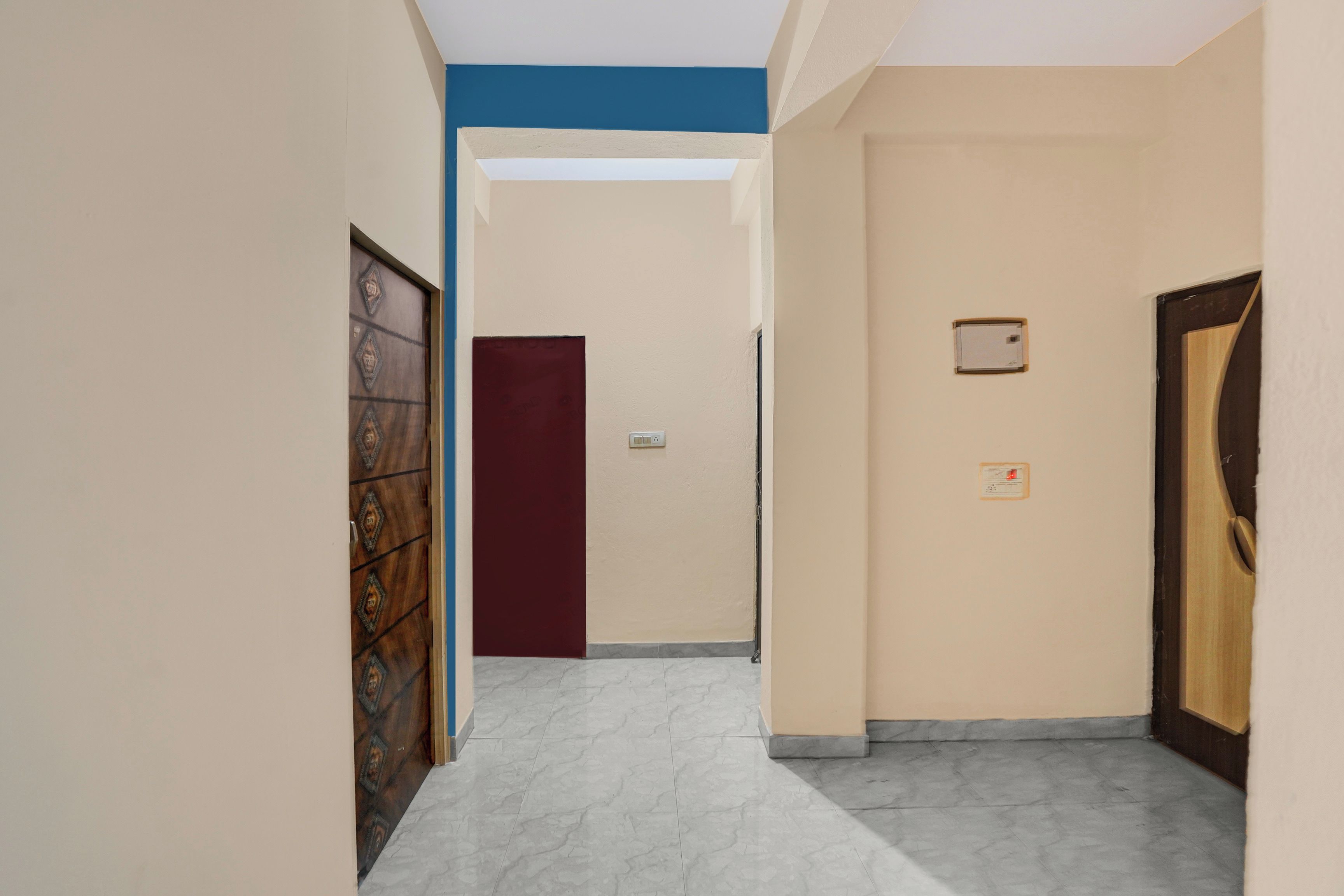 Un couloir doté d’un sol en marbre, d’une porte rouge et d’un mur beige avec une petite prise électrique.
