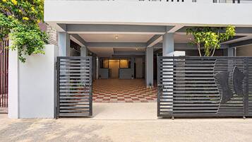 Una entrada de edificio moderno con piso de cuadros, puertas metálicas y un balcón con barandilla.