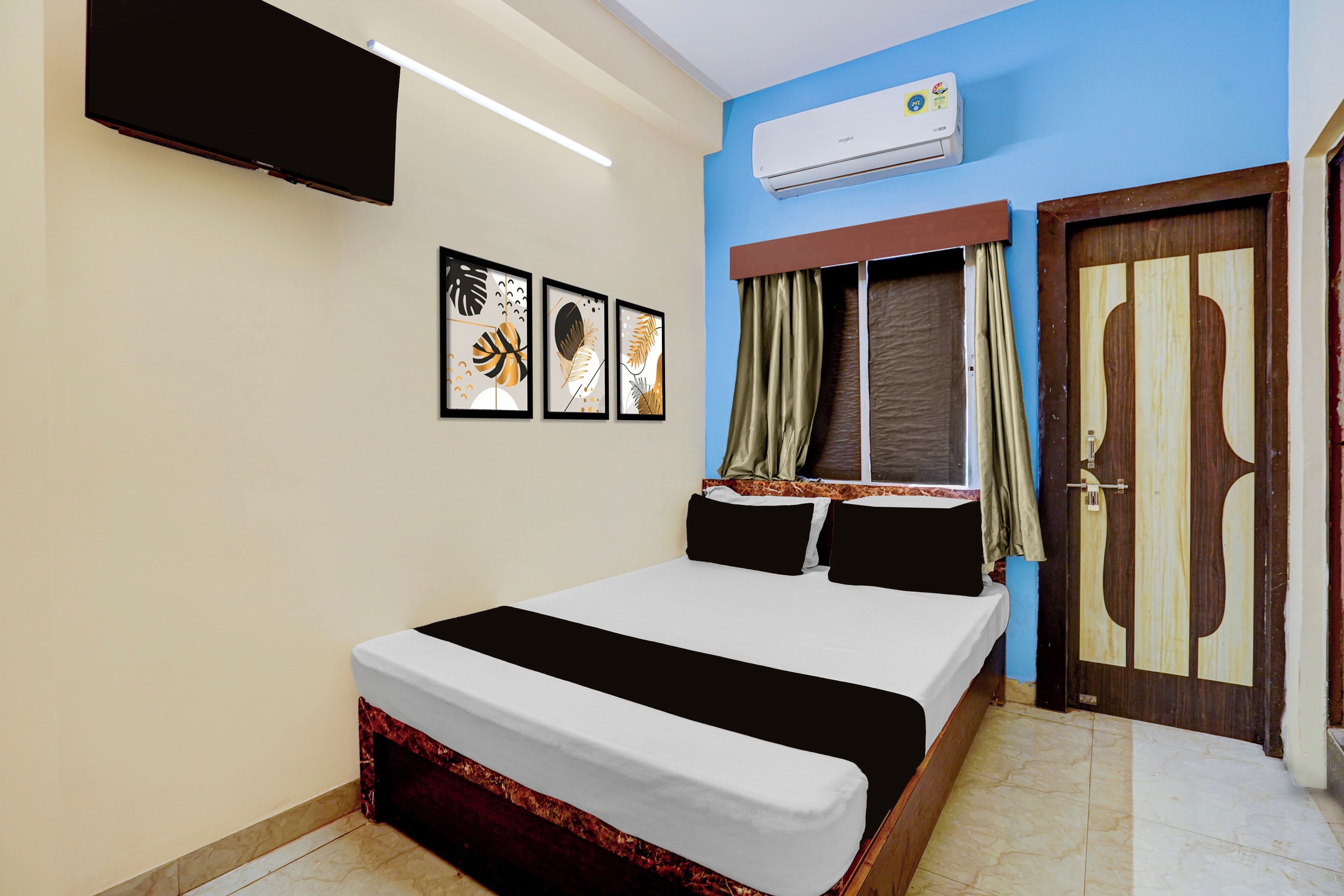 A bedroom with a bed, a flat-screen TV mounted on the wall, and an air conditioning unit above the door.
