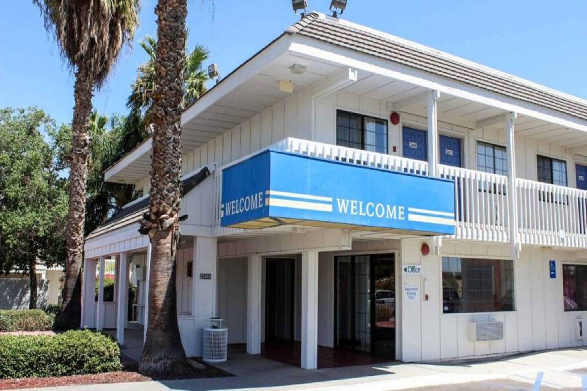 A building with a 'WELCOME' sign, multiple doors, and a parking sign.