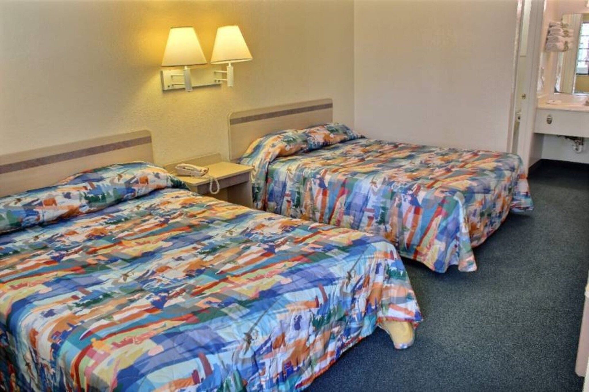 Ein Hotelzimmer mit zwei Betten, jeweils mit bunter Blumenbettwäsche, einem Nachttisch mit Telefon und Wandlampen.
