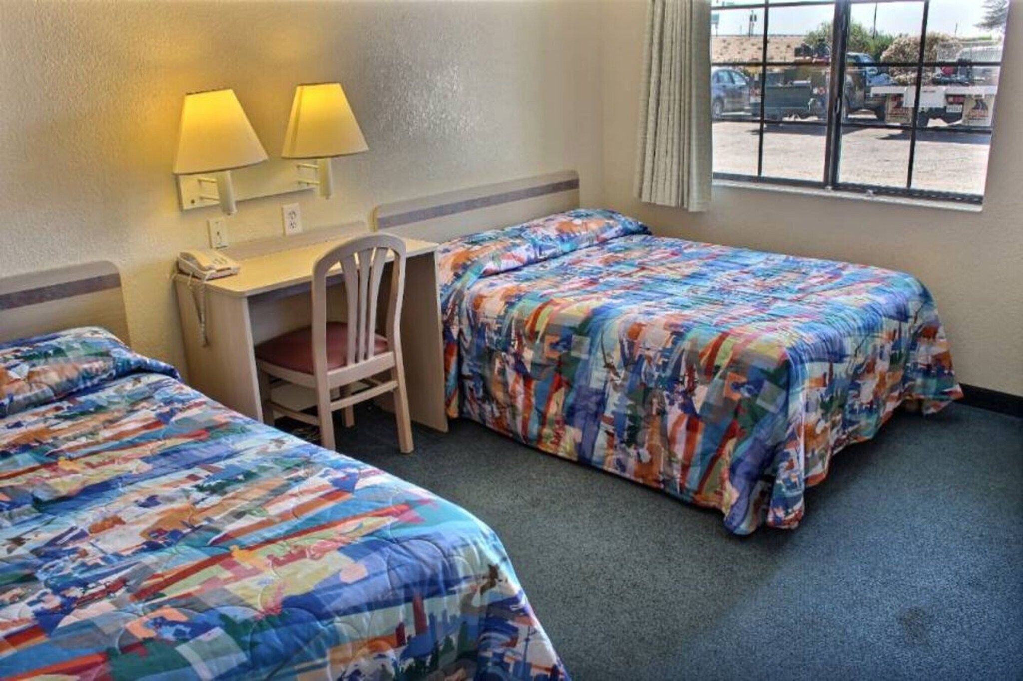 Habitación de hotel con dos camas, un escritorio, una silla y una ventana con vistas al exterior.