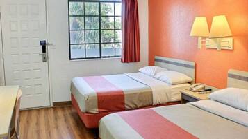 A hotel room with two beds, a window with a view of trees, a door, and a nightstand with a lamp.