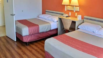 A hotel room with two beds, a desk with a telephone, and a wall-mounted lamp.