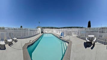 A swimming pool with a clear blue water, surrounded by a white fence, and a small building in the background.