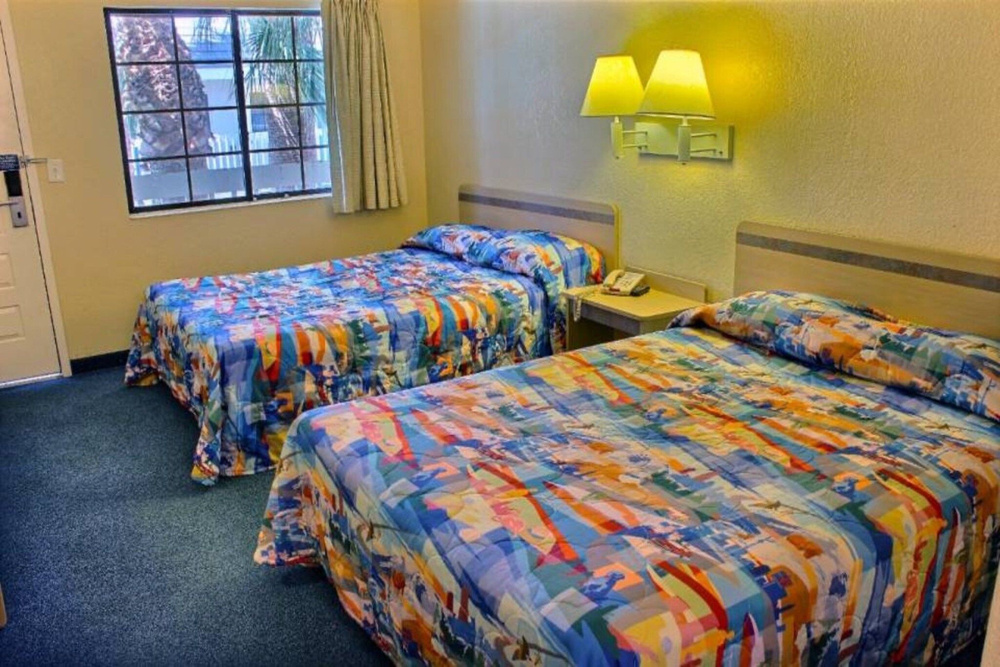 A hotel room with two beds, a window, a lamp, and a telephone.