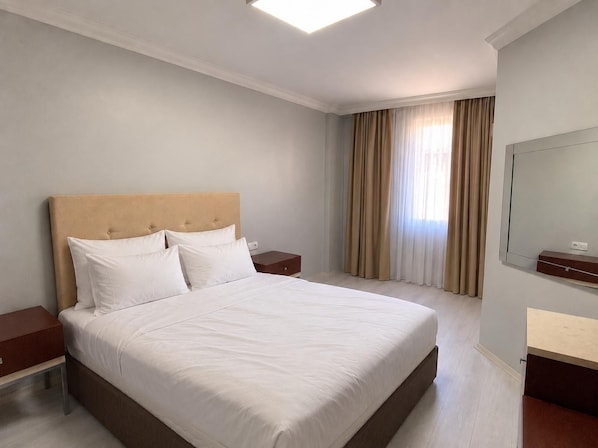 Una habitación de hotel con una cama grande, una mesita de noche, un espejo y una ventana con cortinas.