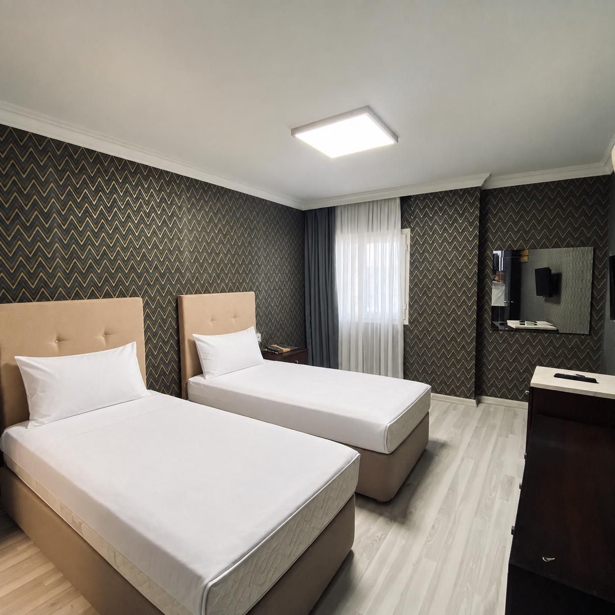 Une chambre d’hôtel avec deux lits, un bureau, un miroir et un luminaire au plafond.