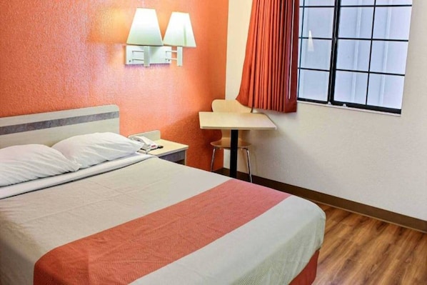 Una habitación de hotel con cama, escritorio, dos lámparas de pared y una ventana con cortinas.