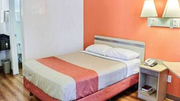 Ein Hotelzimmer mit Bett, Nachttisch, Lampe und Mülleimer.