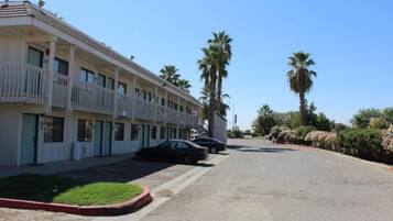 A row of motel buildings with balconies, parked cars, and palm trees.