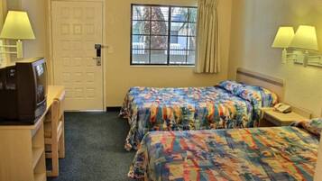A hotel room with two beds, a desk with a television, a window with curtains, and a door.