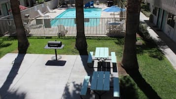 An outdoor pool area with a barbecue grill, picnic tables, and a fenced swimming pool.