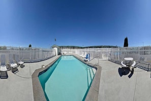 A swimming pool with a clear blue water, surrounded by a white fence, and a small building in the background. - 2 Queen Beds | Mini Fridge (Coalinga CA)