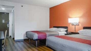 Une chambre d’hôtel avec deux lits, un plancher en bois, une porte blanche et une lampe fixée au mur.