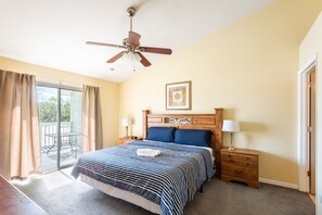 Ein Schlafzimmer mit einem Bett, zwei Nachttischen, einem Deckenventilator, einem Fenster mit Vorhängen und einer Tür.