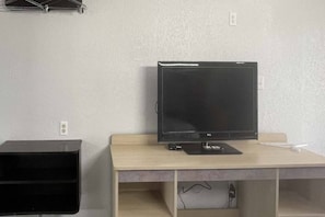 A room with a flat-screen TV on a wooden desk, a black speaker, and a power outlet on the wall.