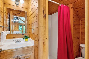 A wooden cabin bathroom with a white sink, mirror, and a red shower curtain. - Sleeps 24 • 2 Cabins • Hot Tubs + Game Rooms + Mtn Views | Bear Ridge Cabins (Gatlinburg)