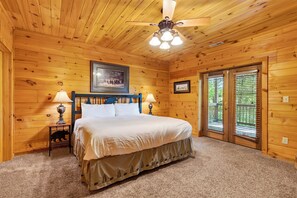 Ein Schlafzimmer einer Holzhütte mit einem Bett, zwei Nachttischlampen, einem Deckenventilator und einem Bild an der Wand.
