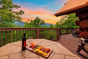 Una terraza de madera con una mesa dispuesta para una comida, una botella de vino y una copa.