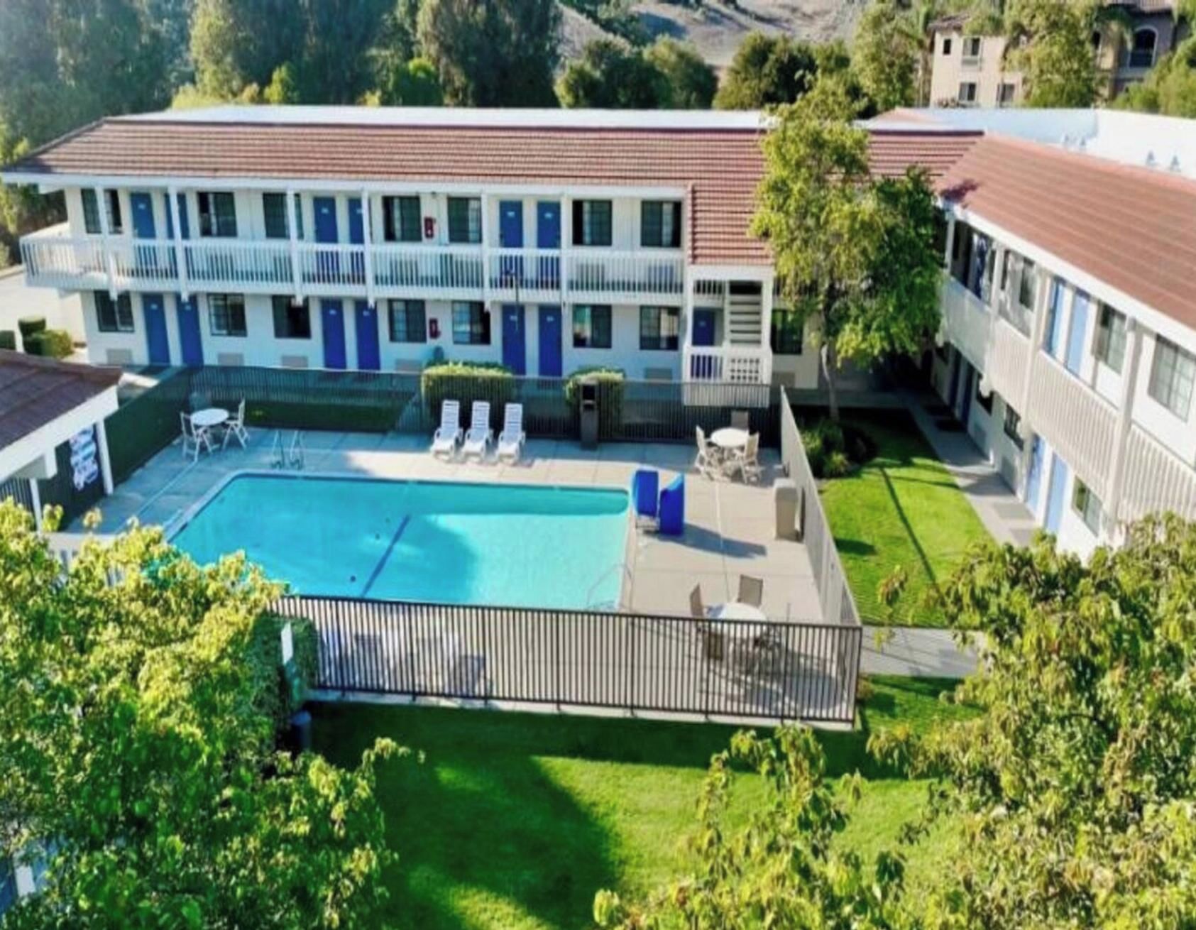 A hotel with a swimming pool, lounge chairs, and a fenced patio area.