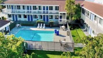 A hotel with a swimming pool, lounge chairs, and a fenced patio area.