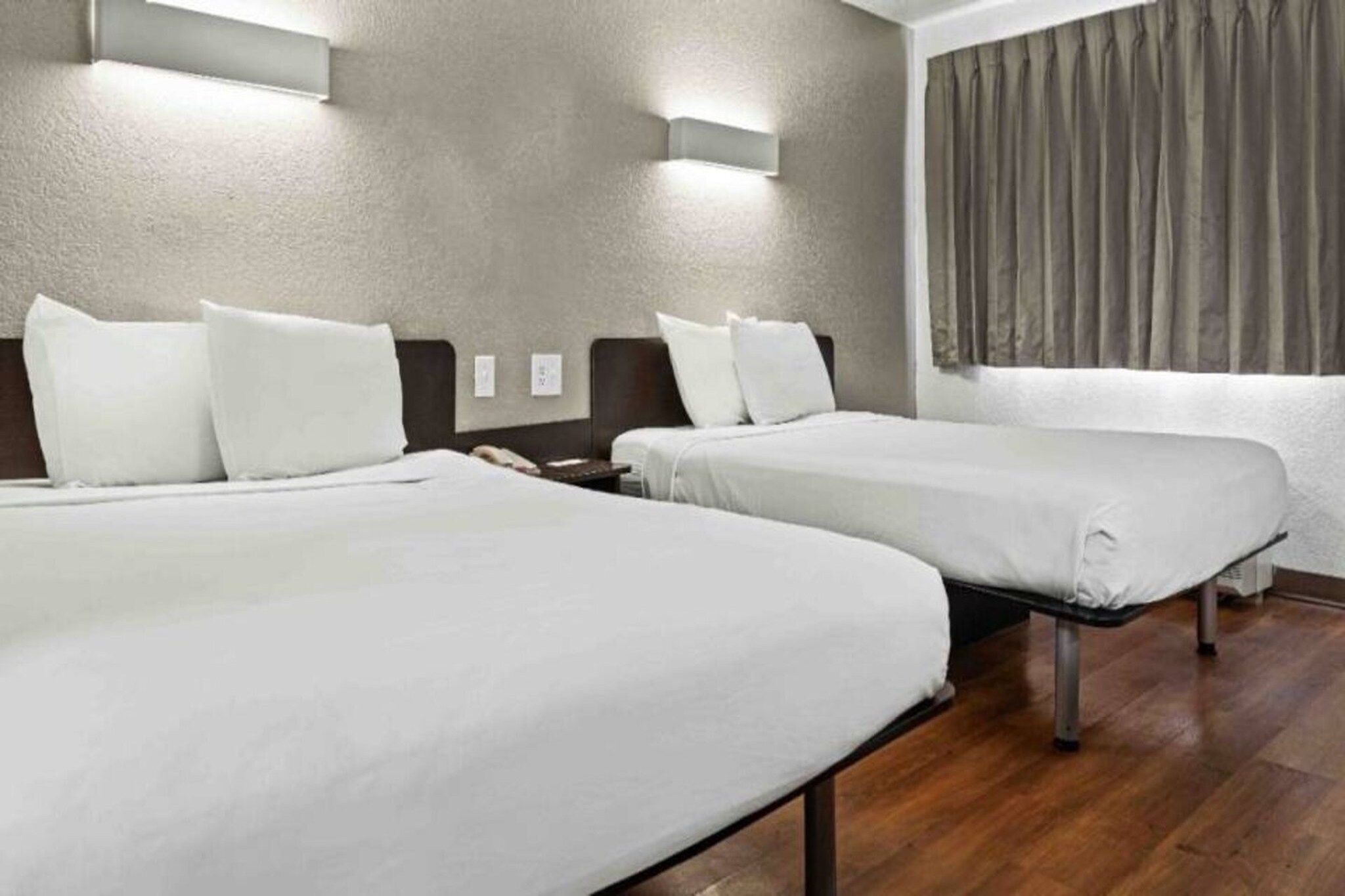 Quarto de hotel com duas camas de solteiro, piso de madeira e cortina na janela.