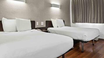 Quarto de hotel com duas camas de solteiro, piso de madeira e cortina na janela.