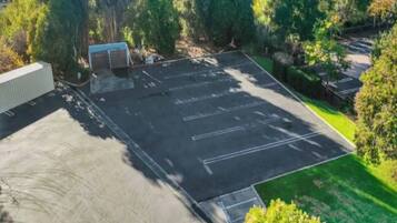 An aerial view of a parking lot with marked spaces, surrounded by greenery and a building.