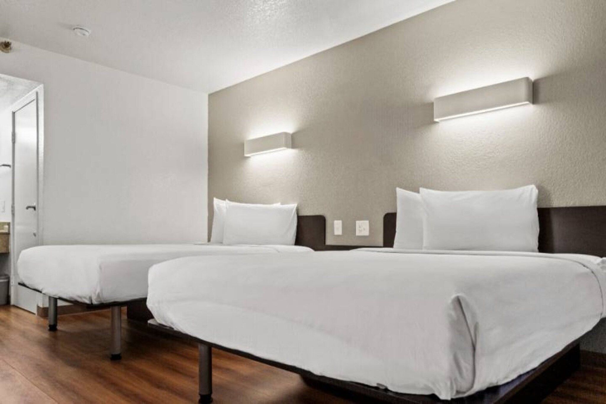 A hotel room with two single beds, wooden flooring, and a door to the left.