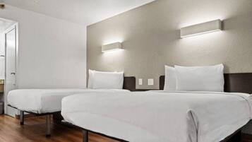 A hotel room with two single beds, wooden flooring, and a door to the left.
