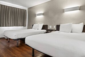 Ein Hotelzimmer mit zwei Betten, einem Fenster mit Vorhängen, Holzboden und Wandleuchten.