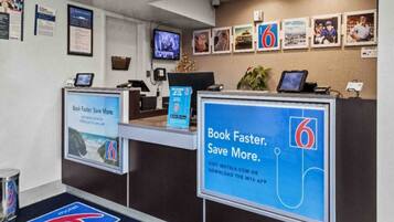 A motel reception desk with a large sign advertising the motel's app, a television, and framed pictures on the wall.