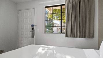 A hotel room with a bed, a window with curtains, and a door.