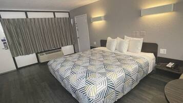 Een hotelkamer met een bed, een bureau, een stoel, een gordijn en een wandlamp.