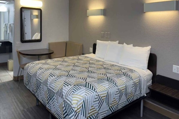 A hotel room with a bed, a small table, a chair, and a mirror. - 1 King Bed | Non-Smoking (Sallisaw)