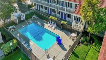 A two-story building with a swimming pool, lounge chairs, and a fenced patio area.