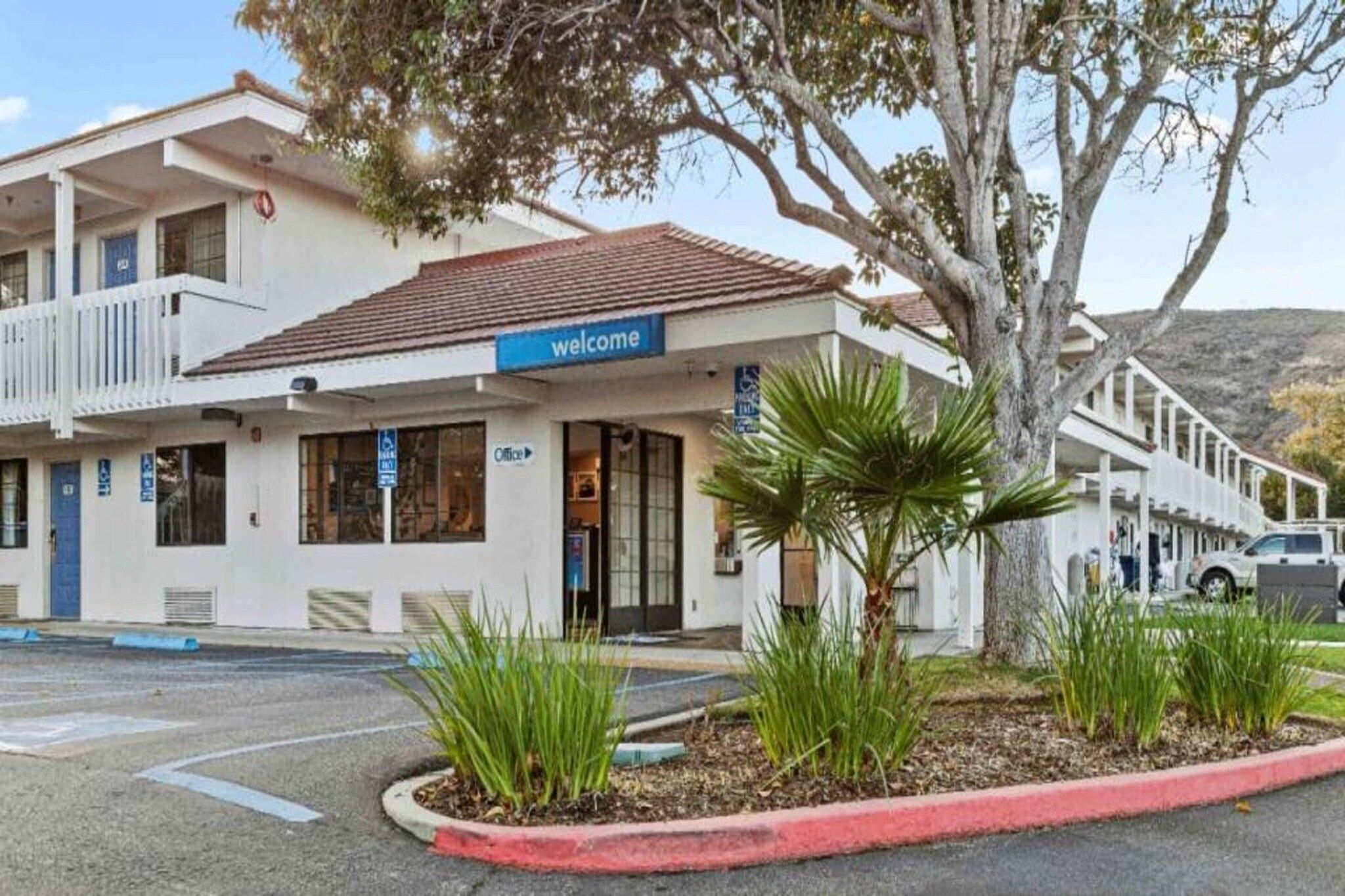 A building with a 'welcome' sign, a parking lot, and a tree.