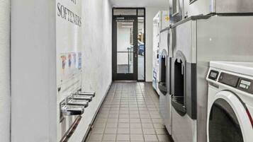 A laundry facility with multiple washing machines and a row of sinks on the left.