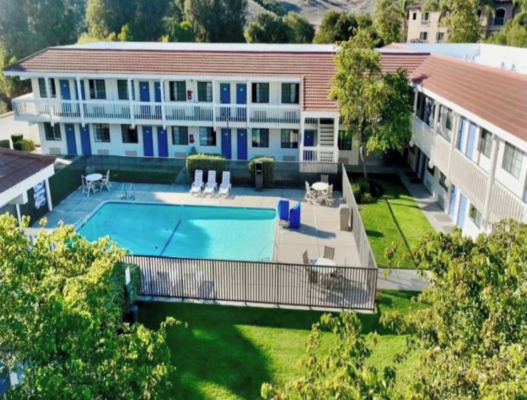 A hotel with a swimming pool, lounge chairs, and a fenced patio area.