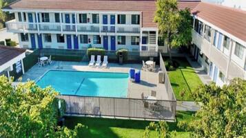 A hotel with a swimming pool, lounge chairs, and a fenced patio area.