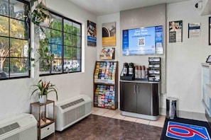 Een kamer met een raam, een plant, een wandplank met boeken, een koelkast en een afvalbak.