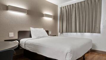 A hotel room with a bed, a desk, and a window with curtains.