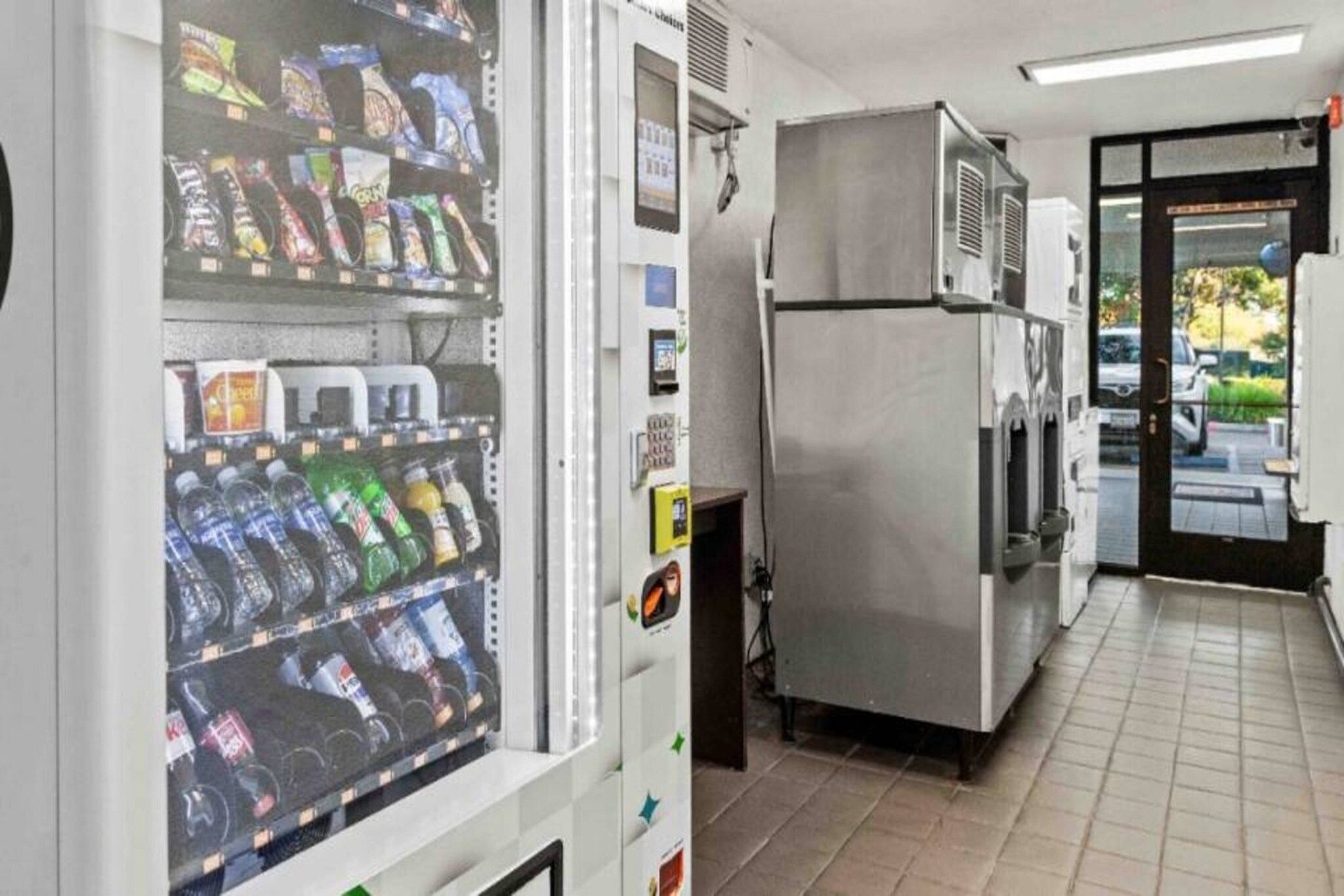 A vending machine with snacks and drinks, a refrigerator, and a door leading outside.