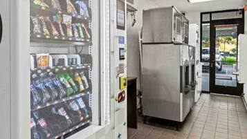 A vending machine with snacks and drinks, a refrigerator, and a door leading outside.
