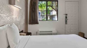 Habitación de hotel con cama, mesita de noche, teléfono, ventana con cortinas y puerta.