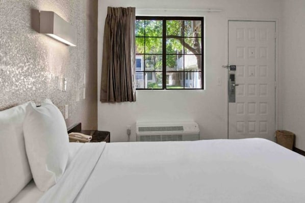 Een hotelkamer met een bed, nachtkastje, telefoon, raam met gordijnen en een deur.