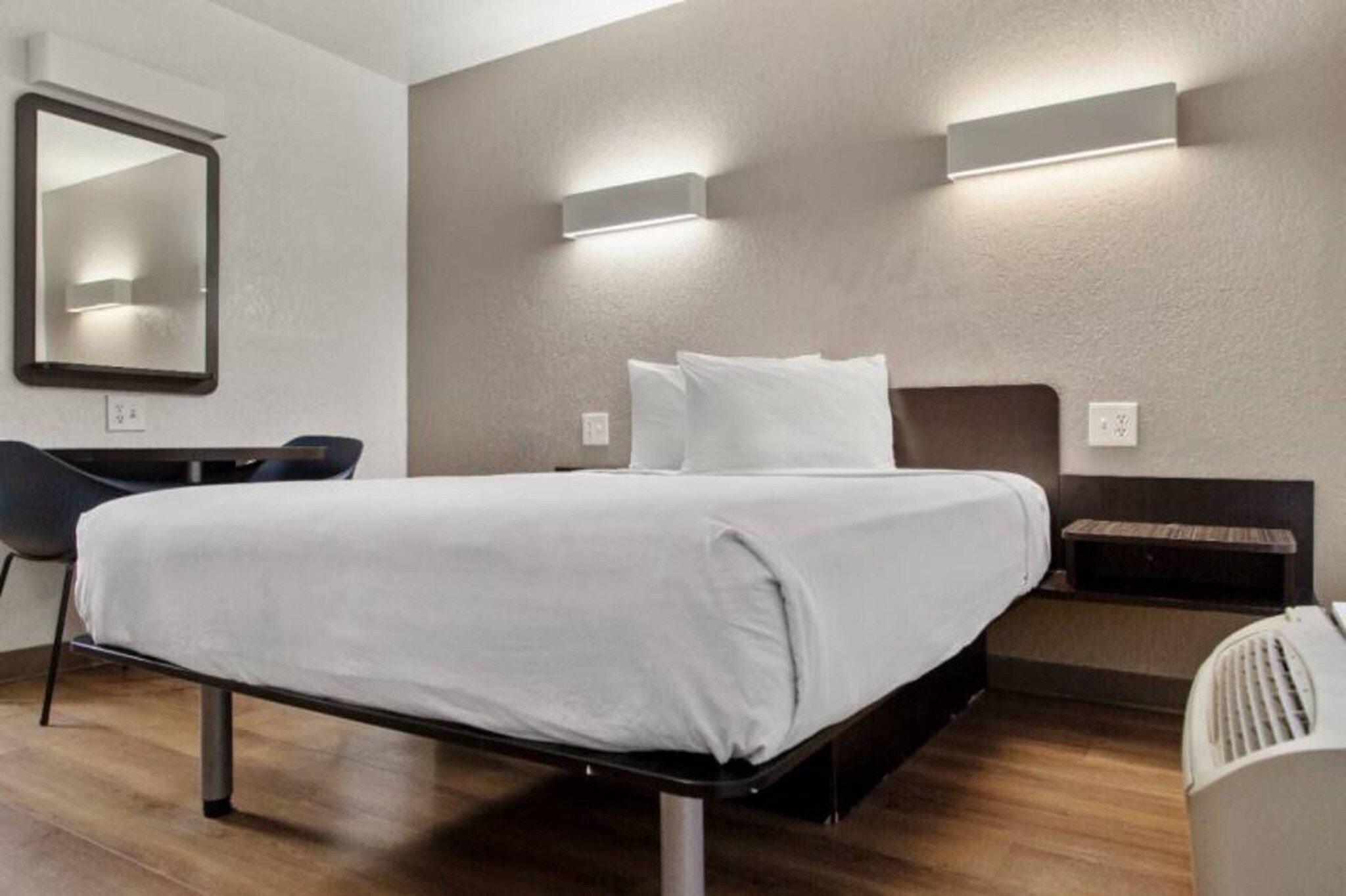 A modern hotel room with a bed, bedside tables, a chair, and a mirror.