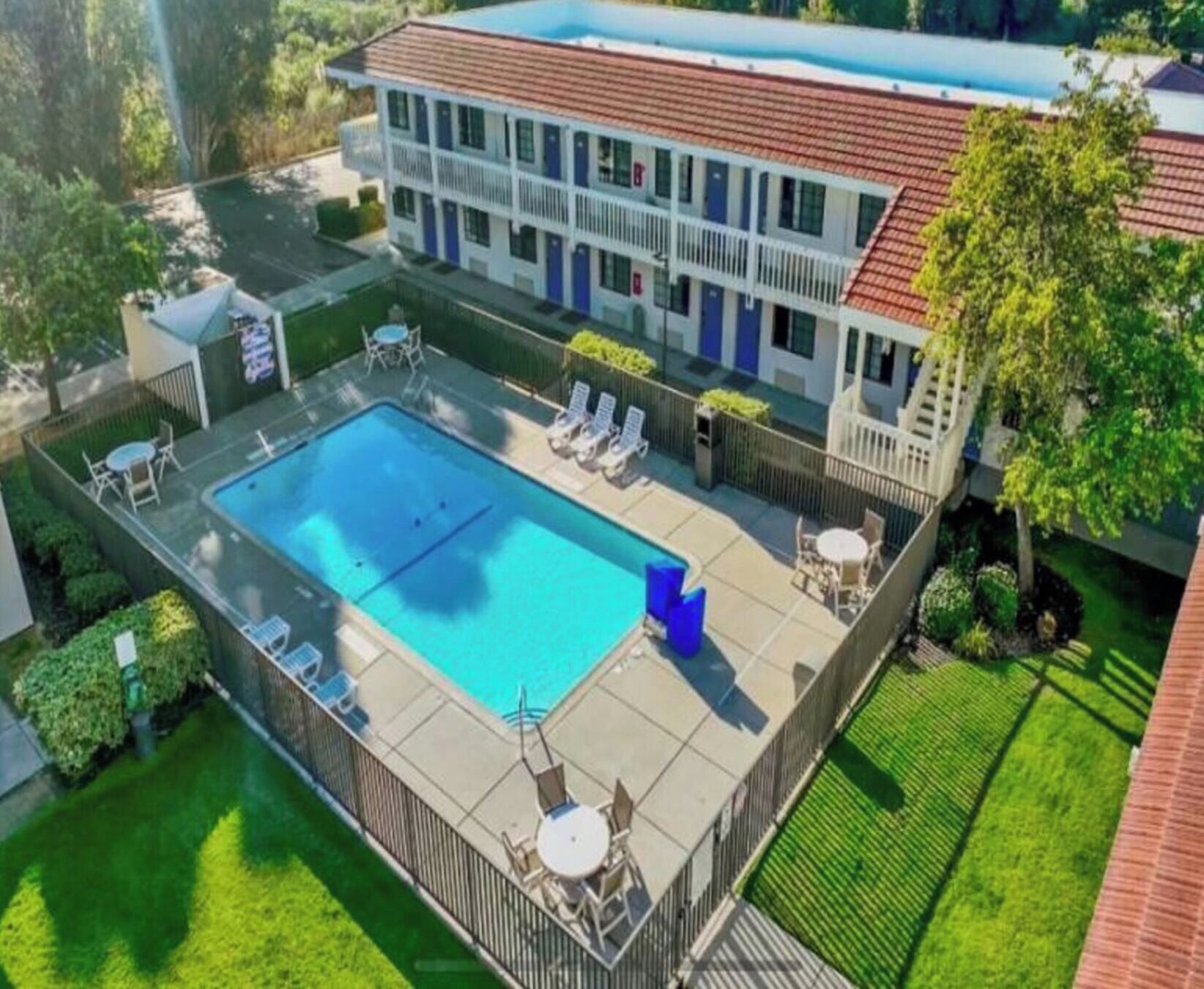 A two-story building with a swimming pool, lounge chairs, and a fenced patio area.